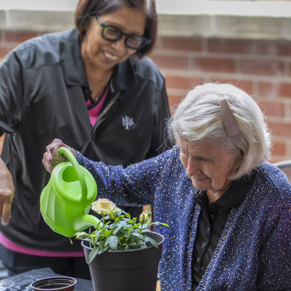 Resident watering flowers with support from a team member during a gardening activity at Atrium Retirement Residence in Orillia