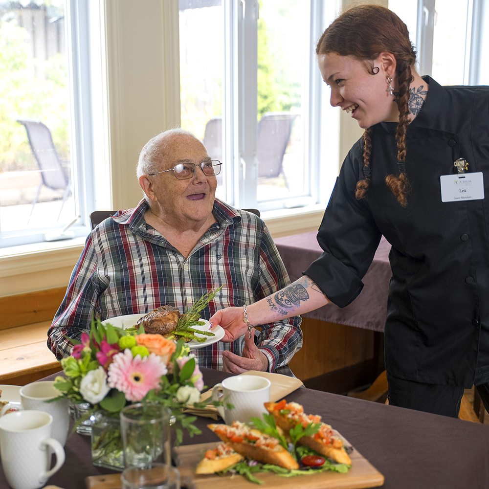 Friendly server bringing a plated meal to a happy resident for dinner.
